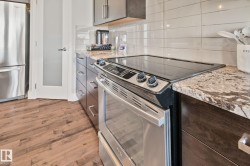 Stainless steel range with a smooth cooktop, wood-finish flooring, dark wood cabinetry, light-toned stone countertops, and a white subway tile backsplash - 