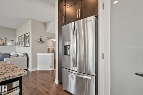 Stainless steel French door refrigerator, dark wood-finish cabinetry with gold-tone hardware, wood-finish flooring, and light-toned countertops - 2096 Redtail Common Nw, Edmonton, AB 
