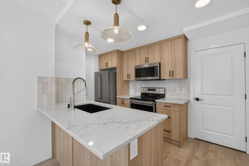 Kitchen featuring a waterfall-edge island, wood-finish cabinetry, stainless steel appliances, and white tiled backsplash - #58 16231 19 Av Sw, Edmonton, AB 