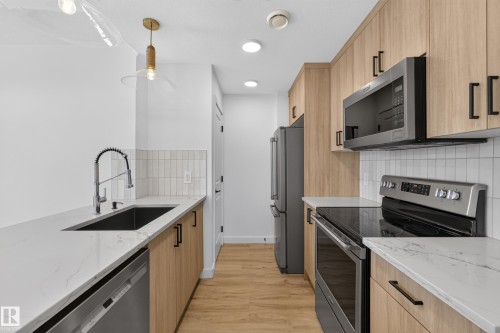 Galley kitchen featuring light wood-finish cabinetry, stainless steel appliances, white countertops, and a subway tile backsplash - #58 16231 19 Av Sw, Edmonton, AB 