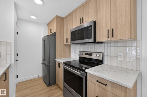 Wood-finish cabinetry paired with light countertops, stainless steel appliances, and a tiled backsplash - #58 16231 19 Av Sw, Edmonton, AB 