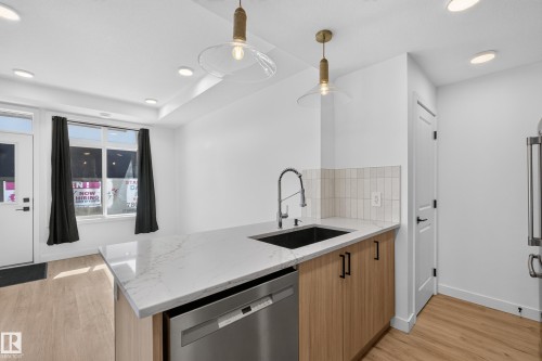 Kitchen island with a light-toned countertop, stainless steel appliances, wood-finish flooring, and pendant lighting - #58 16231 19 Av Sw, Edmonton, AB 
