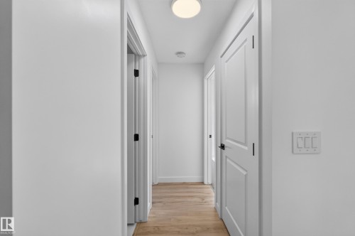 Hallway featuring wood-finish flooring, white walls, flush-mount ceiling light, and white paneled doors with dark hardware - #58 16231 19 Av Sw, Edmonton, AB 