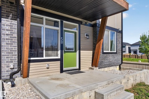 Front entry with a vibrant green door, contrasting dark brick and tan siding, and a concrete stoop with steps - #58 16231 19 Av Sw, Edmonton, AB 