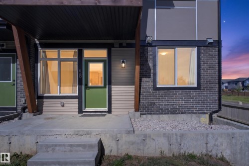 Modern exterior with a green entry door, concrete patio, dark brick accents, and horizontal siding - #58 16231 19 Av Sw, Edmonton, AB 