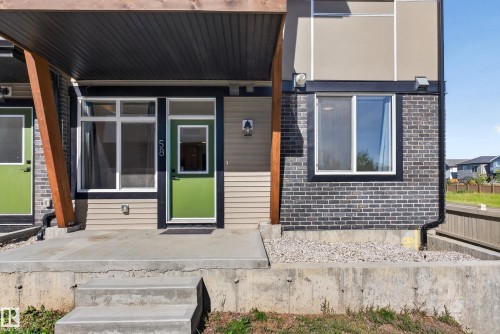 Exterior featuring a concrete entry, vibrant green entry door, multiple windows, and a dark brick facade - #58 16231 19 Av Sw, Edmonton, AB 
