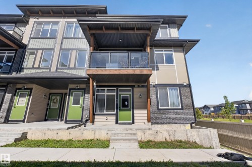 Modern multi-level exterior with a balcony featuring glass railings, multiple windows, and a prominent front entrance with a bright door - #58 16231 19 Av Sw, Edmonton, AB 