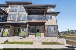 Modern multi-level exterior with a balcony featuring glass railings, multiple windows, and a prominent front entrance with a bright door - 