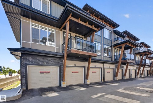 Modern townhome exterior with multiple balconies featuring glass railings, individual garage doors, wood beam accents, and varied siding materials - #58 16231 19 Av Sw, Edmonton, AB 