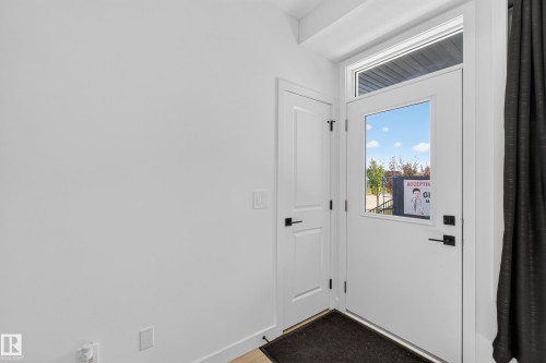 White entry door with a glass insert and transom window, accompanied by a white interior door with black hardware, all set against white walls - #58 16231 19 Av Sw, Edmonton, AB 