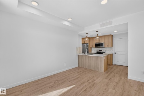 Kitchen featuring wood-finish cabinetry, stainless steel appliances, white subway tile backsplash, and a breakfast bar with pendant lighting - #58 16231 19 Av Sw, Edmonton, AB 