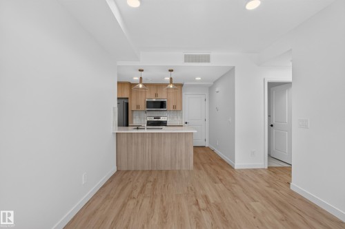 Open-concept kitchen with wood-finish flooring, light wood cabinetry, stainless steel appliances, and pendant lighting - #58 16231 19 Av Sw, Edmonton, AB 