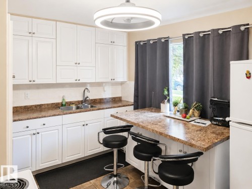 White cabinetry, dual basin stainless steel sink, patterned countertop, tile backsplash, and overhead lighting fixture - 12130 124 Street Nw, Edmonton, AB 