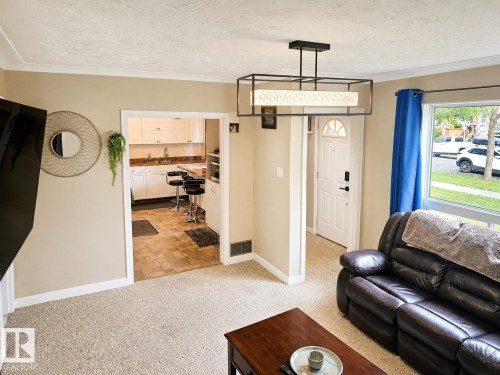 Expansive living area with neutral carpeting, crown molding, and a modern rectangular chandelier - 12130 124 Street Nw, Edmonton, AB 