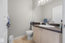Recessed lighting fixture, light gray walls, vanity with wood-finish cabinetry, dark countertop, and integrated white sink, ceramic tile flooring - 