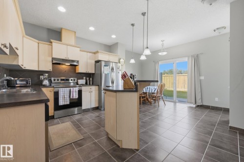 Kitchen featuring wood-finish cabinetry, stainless steel appliances, a center island with bar seating, and tile flooring - #102 13825 155 Av Nw, Edmonton, AB 