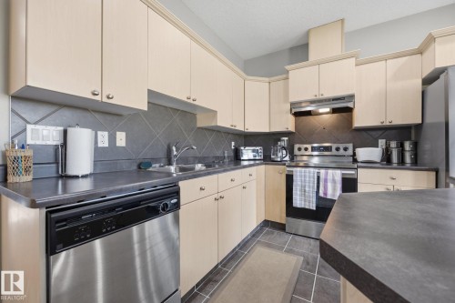 Kitchen featuring light wood-finish cabinetry, stainless steel dishwasher, stainless steel range, and tile backsplash - #102 13825 155 Av Nw, Edmonton, AB 
