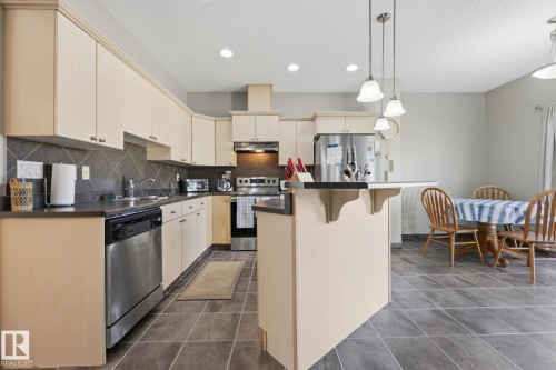 Kitchen featuring light-toned cabinetry, dark countertops, and stainless steel appliances - #102 13825 155 Av Nw, Edmonton, AB 