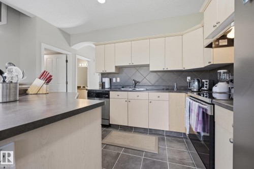 Kitchen featuring pale wood-finish cabinetry, dark tile flooring, a dark diamond-patterned tile backsplash, and a dark countertop - #102 13825 155 Av Nw, Edmonton, AB 