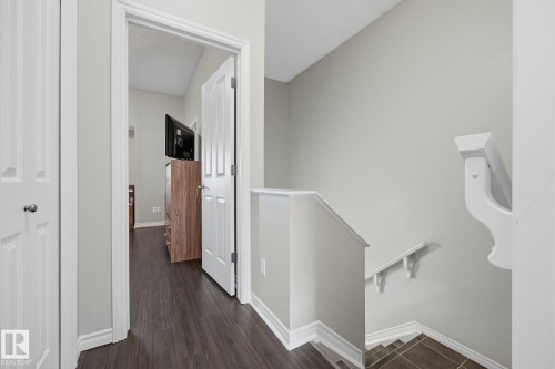 Hallway with dark wood-finish flooring, white trim, and a white paneled door - #102 13825 155 Av Nw, Edmonton, AB 