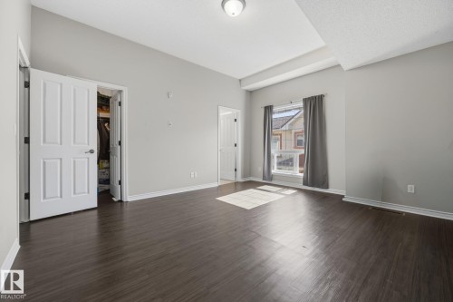 Tray ceiling detail, dark wood-finish flooring, white trim, window with natural light, and a built-in closet - #102 13825 155 Av Nw, Edmonton, AB 