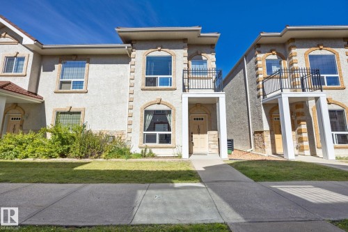 Stucco exterior with stone accents, arched windows, and a second-story balcony with metal railing - #102 13825 155 Av Nw, Edmonton, AB 