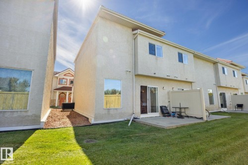 Expansive backyard featuring a manicured lawn, concrete patio, and sliding glass door access - #102 13825 155 Av Nw, Edmonton, AB 