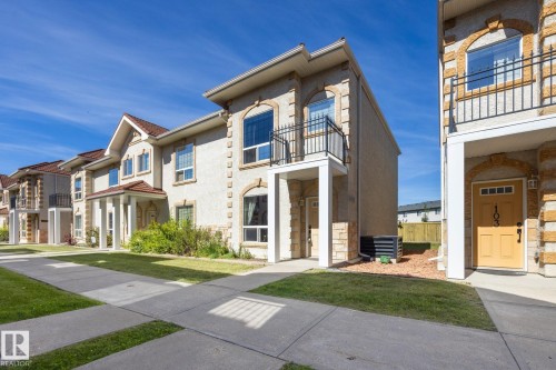 Stucco exterior with stone accents, arched windows, second-story balcony with metal railing, and covered entry - #102 13825 155 Av Nw, Edmonton, AB 