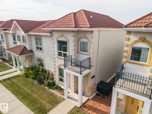 Stucco exterior with stone accents, tile roofing, upper-level balcony with wrought iron railing, covered entry, and front yard landscaping - #102 13825 155 Av Nw, Edmonton, AB 