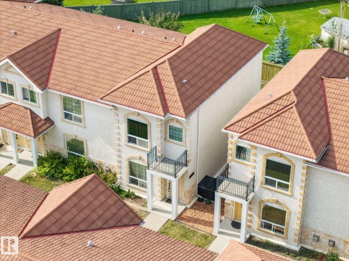 Stucco exterior with stone accents, arched window casings, terracotta-toned tile roofing, and upper-level balconies with wrought iron railings - #102 13825 155 Av Nw, Edmonton, AB 