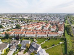 Aerial perspective showcasing a residential community with red-tiled roofs, a large grass area, and a distant city skyline - 