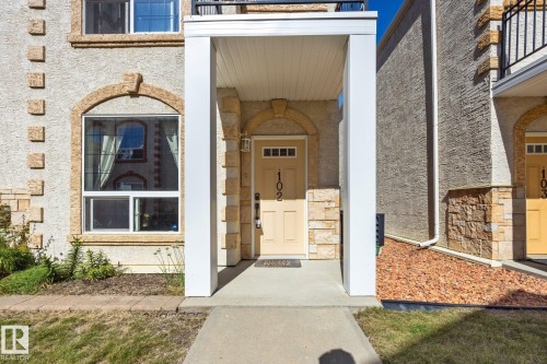 Stucco exterior with stone accents, arched window and doorway details, covered entry, and paved walkway - #102 13825 155 Av Nw, Edmonton, AB 