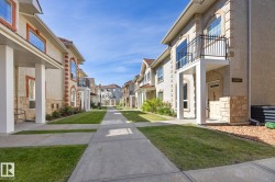 Stucco exterior with stone accents, arched windows, second-story balcony with iron railing, and concrete pathways with integrated lawn - 