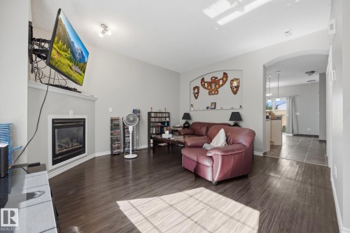 Vaulted ceiling with track lighting, wood-finish flooring, and a fireplace with a mantel - #102 13825 155 Av Nw, Edmonton, AB 