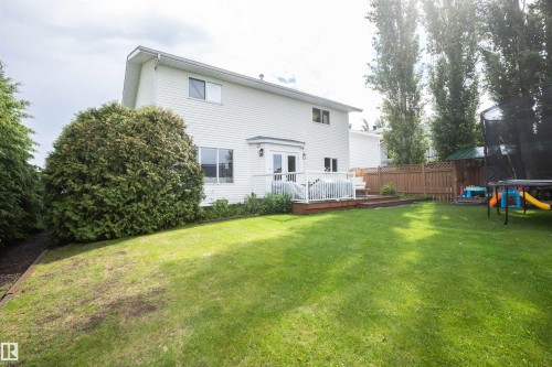 Expansive rear yard featuring a large wooden deck with white railing, double French doors, mature perimeter trees, and a wooden privacy fence - 5502 60 Avenue, Barrhead, AB - Outdoor