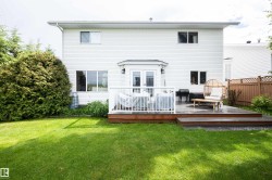 Expansive rear yard featuring a multi-level wood deck with white railings, a stone patio, and a large green lawn - 