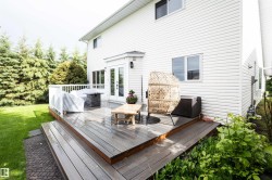 Elevated outdoor deck with composite decking, featuring white railing, direct access via French doors, and a surrounding green lawn with mature evergreen trees - 