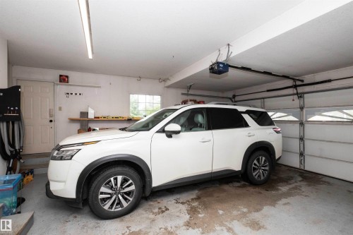 Attached garage featuring a white overhead door with window panels, multiple fluorescent light fixtures, an automatic garage door opener, and a built-in workbench with shelving - 5502 60 Avenue, Barrhead, AB - Indoor Photo Showing Garage