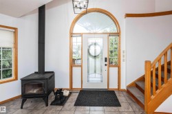 Entryway featuring a decorative arched glass-paneled door with sidelights, tile flooring, and a black freestanding wood-burning stove - 