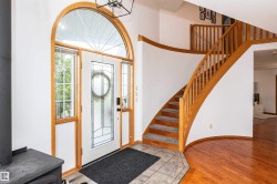 Grand entryway featuring a curved staircase with natural wood railing and an arched transom window above the front door - 