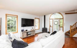 Inviting living area featuring rich wood-finish flooring, a contemporary wood-burning stove, and multiple windows with natural wood trim - 