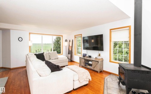 Spacious living area featuring wood-finish flooring, a freestanding wood-burning fireplace with a tile hearth, and multiple windows with wood trim - 5502 60 Avenue, Barrhead, AB - Indoor Photo Showing Living Room