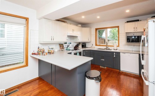 Kitchen featuring wood-finish flooring, two-tone cabinetry, and light-toned countertops - 5502 60 Avenue, Barrhead, AB - Indoor Photo Showing Kitchen With Double Sink