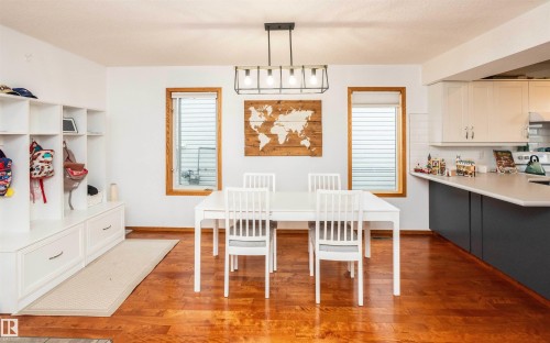 Open-concept dining area featuring wood-finish flooring, a contemporary linear chandelier, and two large windows with natural wood trim - 5502 60 Avenue, Barrhead, AB - Indoor