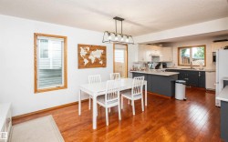Open-concept living space featuring wood-finish flooring, a contemporary linear chandelier, and a kitchen with two-tone cabinetry - 