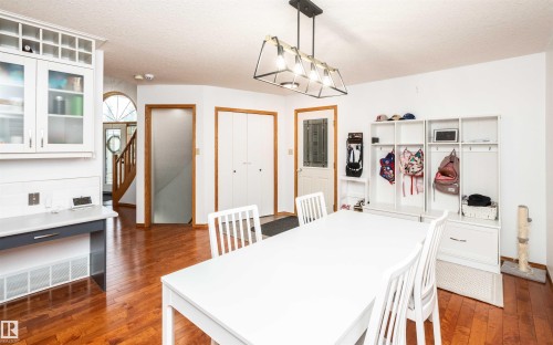 Dining area featuring wood-finish flooring, a contemporary linear chandelier, and white shaker-style cabinetry with glass inserts - 5502 60 Avenue, Barrhead, AB - Indoor Photo Showing Other Room