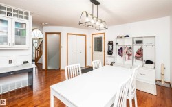 Dining area featuring wood-finish flooring, a contemporary linear chandelier, and white shaker-style cabinetry with glass inserts - 