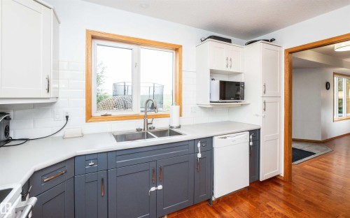 Kitchen featuring a two-tone cabinetry design with white upper cabinets and dark gray lower cabinets, white subway tile backsplash, and a light-colored countertop - 5502 60 Avenue, Barrhead, AB - Indoor Photo Showing Kitchen With Double Sink