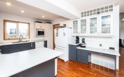 Kitchen featuring a central island, wood-finish flooring, white cabinetry with frosted glass inserts, and contrasting dark base cabinets - 