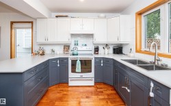 Kitchen featuring wood-finish flooring, two-tone cabinetry with white upper and blue-gray lower units, white countertops, and a white subway tile backsplash - 